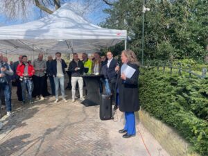 Wethouder Esther Heutink-Wenderich voorziet de feestelijke opening van een speech. Onder een partytent luisteren de toeschouwers.